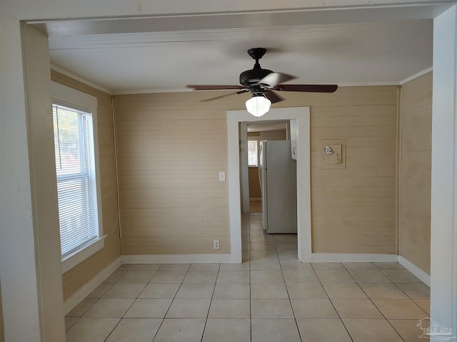 tiled spare room featuring ornamental molding, a healthy amount of sunlight, ceiling fan, and wooden walls