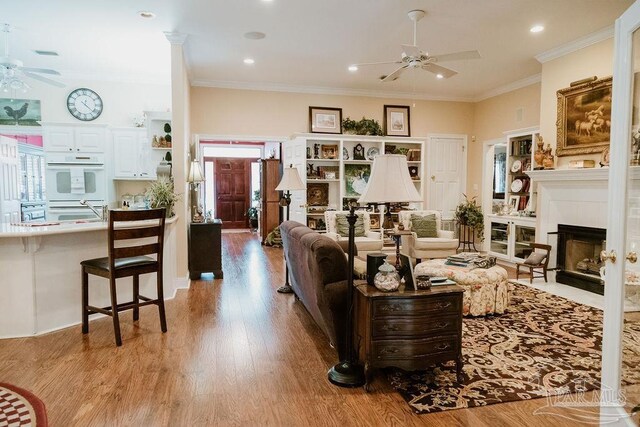 living room with ceiling fan, ornamental molding, light hardwood / wood-style flooring, and a fireplace