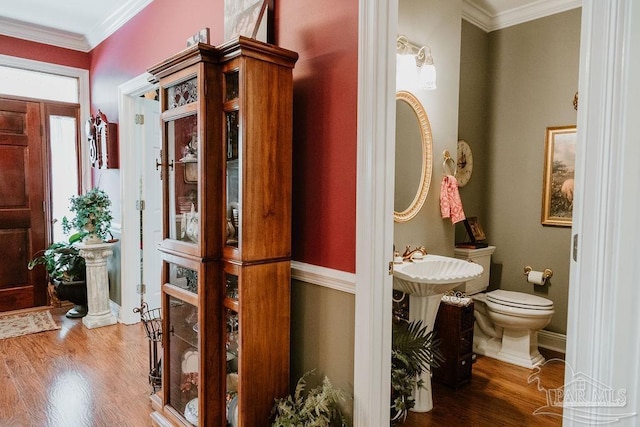 bathroom featuring toilet, baseboards, crown molding, and wood finished floors