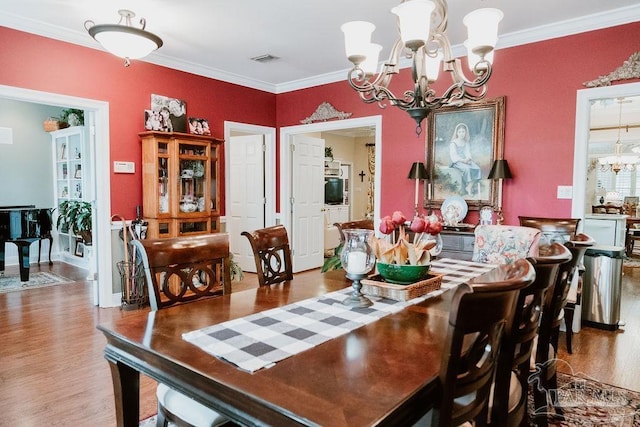 dining space featuring crown molding, visible vents, a notable chandelier, and wood finished floors