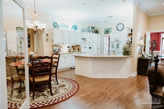 kitchen with a peninsula, white appliances, light countertops, ornamental molding, and light wood finished floors