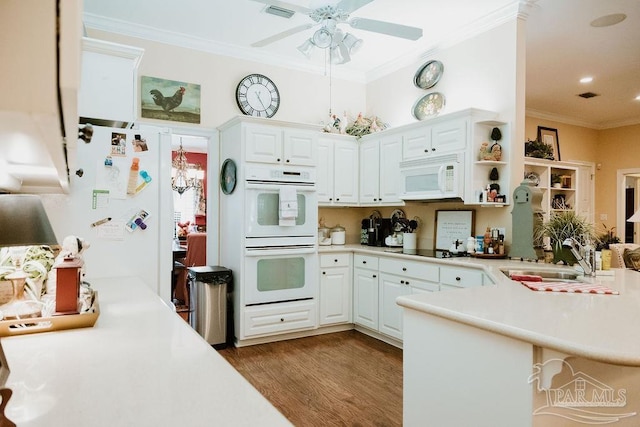 kitchen with white appliances, visible vents, ornamental molding, a peninsula, and a sink