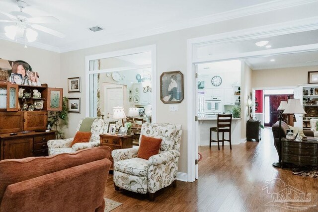 sitting room featuring ceiling fan, visible vents, baseboards, dark wood finished floors, and crown molding