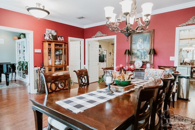 dining space with hardwood / wood-style flooring, ornamental molding, and a chandelier