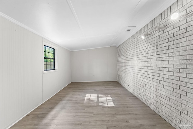 unfurnished room with light wood-type flooring, brick wall, and ornamental molding