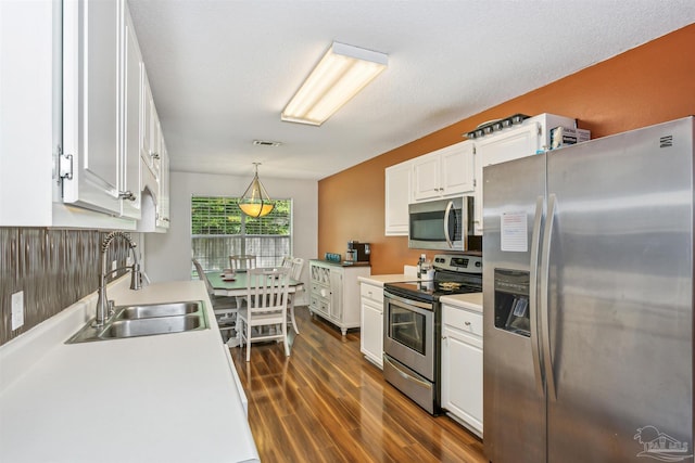 kitchen featuring stainless steel appliances, pendant lighting, white cabinets, sink, and dark wood-type flooring