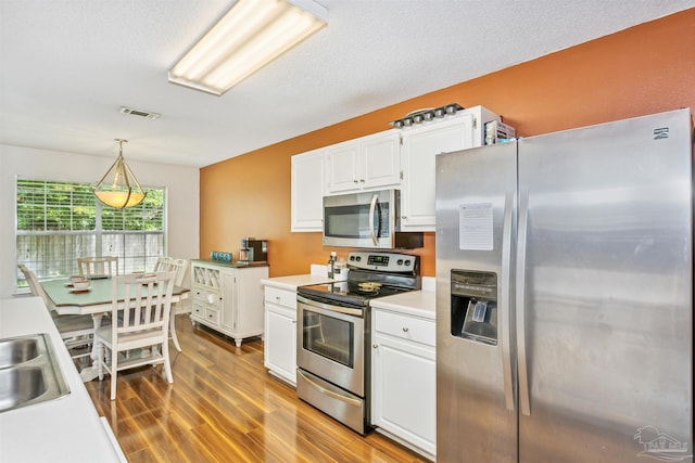 kitchen with white cabinets, pendant lighting, stainless steel appliances, hardwood / wood-style flooring, and sink