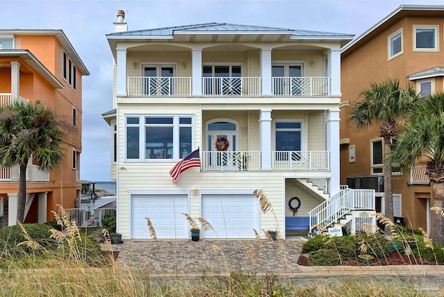 view of front of property featuring metal roof, cooling unit, a balcony, a garage, and decorative driveway