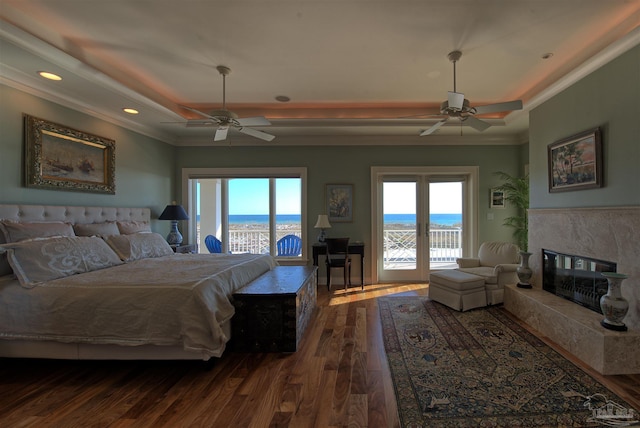 bedroom featuring access to exterior, a tray ceiling, dark wood-style floors, a water view, and a premium fireplace