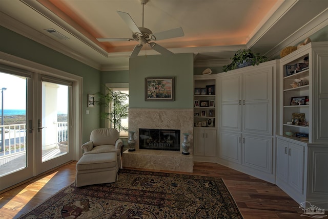 living area with french doors, a raised ceiling, visible vents, a premium fireplace, and wood finished floors