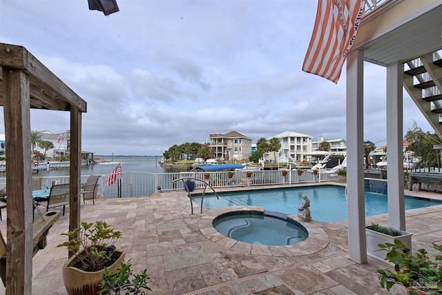 view of pool with a water view, a pool with connected hot tub, fence, and a patio