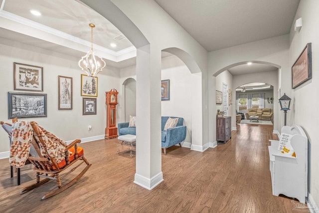 interior space featuring baseboards, arched walkways, a raised ceiling, and wood finished floors