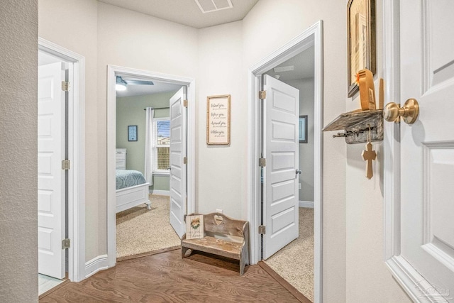 hall with wood finished floors, visible vents, and baseboards