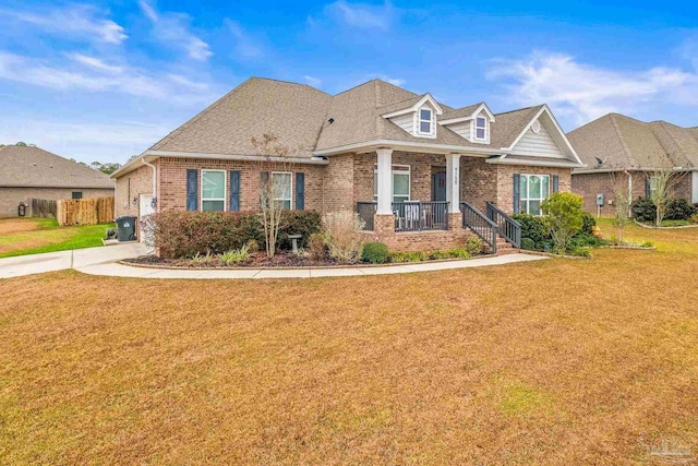 view of front of home featuring covered porch, brick siding, roof with shingles, and a front yard