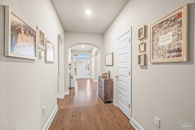 hallway featuring arched walkways, wood finished floors, and baseboards