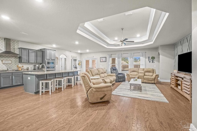 living room featuring a tray ceiling, recessed lighting, ornamental molding, ceiling fan, and light wood-type flooring