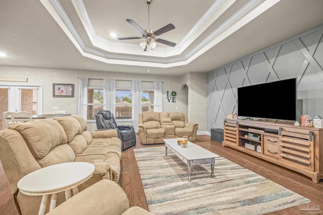 living area with a raised ceiling, ceiling fan, wood finished floors, crown molding, and french doors