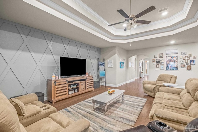 living room featuring arched walkways, a raised ceiling, visible vents, ornamental molding, and wood finished floors