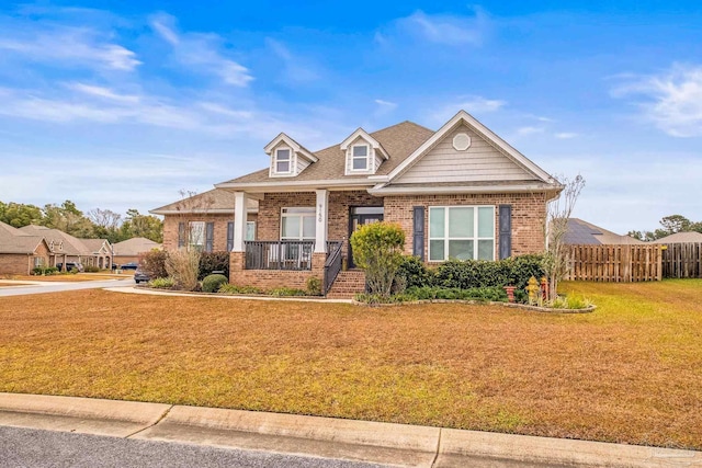 view of front of house with a front yard, covered porch, brick siding, and fence