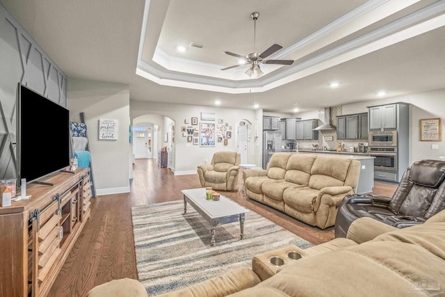 living room with arched walkways, visible vents, dark wood-style floors, a tray ceiling, and crown molding