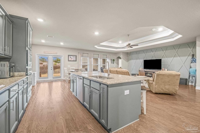 kitchen with open floor plan, gray cabinets, a raised ceiling, and a kitchen island with sink