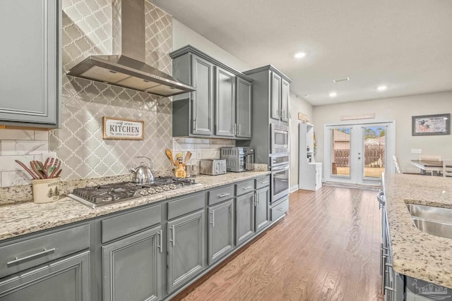 kitchen with wall chimney range hood, light wood-style flooring, appliances with stainless steel finishes, and gray cabinetry