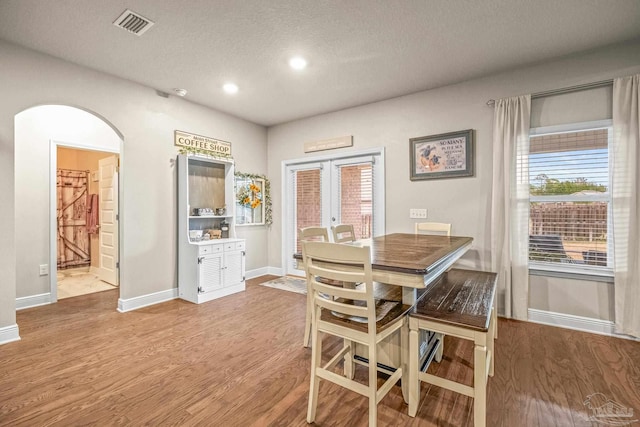 dining room with arched walkways, french doors, wood finished floors, and visible vents