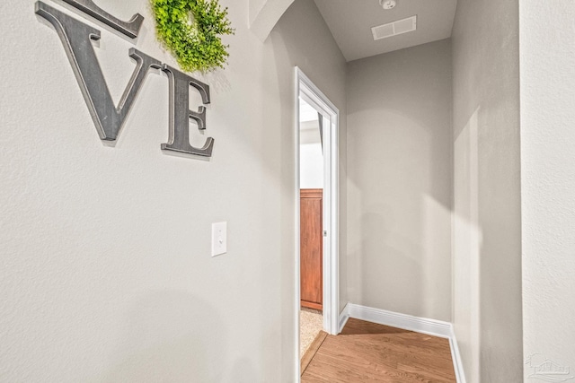 hall with wood finished floors, visible vents, and baseboards