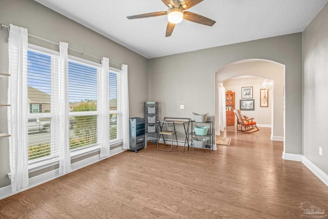 living area featuring light wood-type flooring, arched walkways, ceiling fan, and baseboards