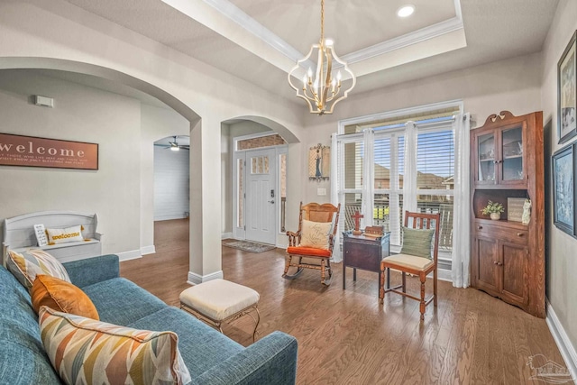 living area featuring crown molding, arched walkways, a raised ceiling, and wood finished floors