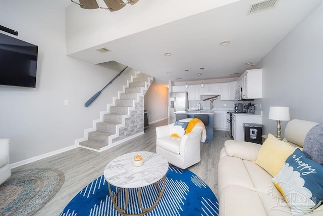 living area with stairway, light wood-type flooring, visible vents, and baseboards