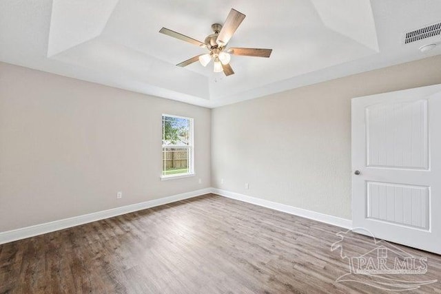 spare room with hardwood / wood-style flooring, ceiling fan, and a raised ceiling