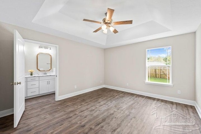 unfurnished bedroom with ceiling fan, dark wood-type flooring, connected bathroom, and a tray ceiling