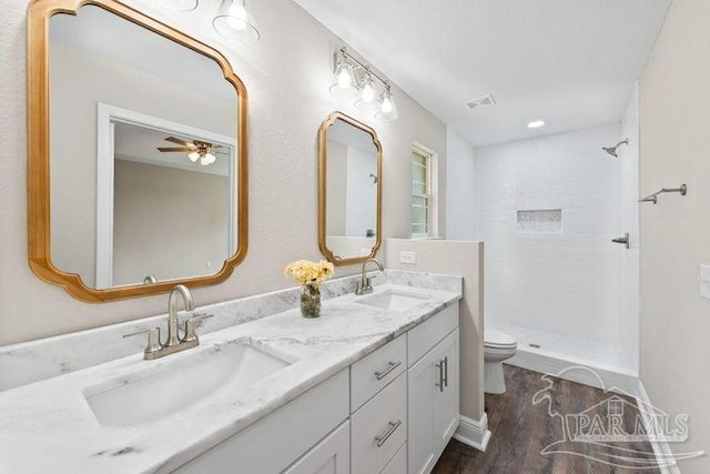 bathroom featuring ceiling fan, wood-type flooring, tiled shower, toilet, and vanity