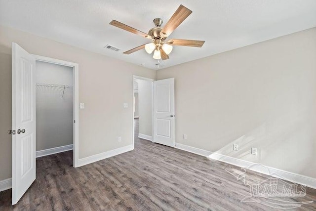 unfurnished bedroom featuring a closet, a spacious closet, ceiling fan, and dark wood-type flooring