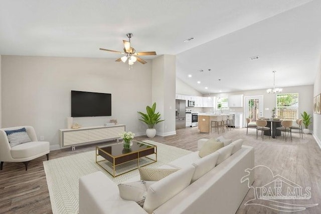 living room featuring lofted ceiling, wood-type flooring, and ceiling fan with notable chandelier