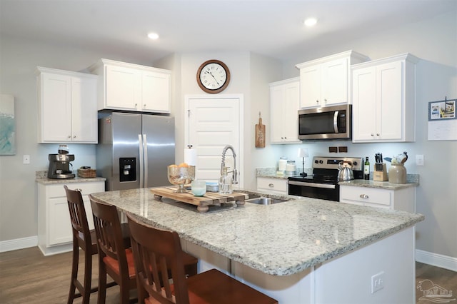 kitchen with white cabinets, appliances with stainless steel finishes, a kitchen breakfast bar, and an island with sink