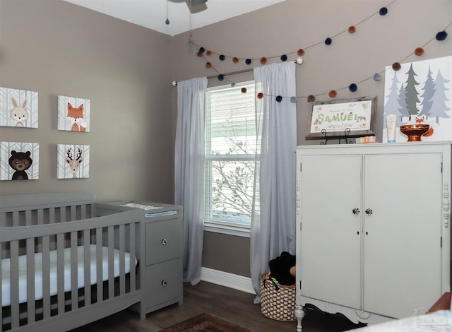 bedroom featuring ceiling fan, dark wood-type flooring, and a crib