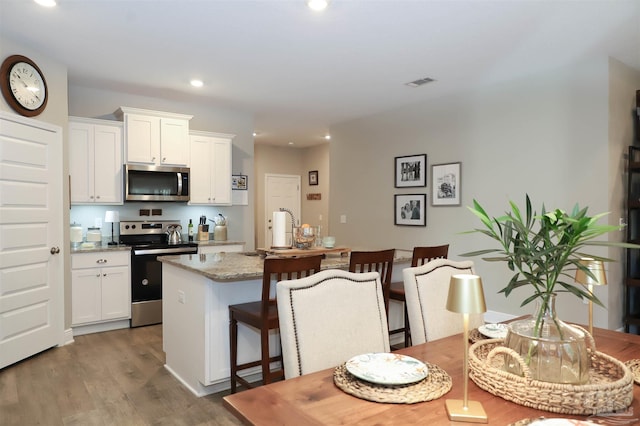 kitchen featuring a kitchen island with sink, white cabinetry, stainless steel appliances, and light stone counters