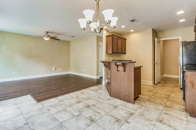 kitchen featuring light tile patterned flooring, a kitchen bar, stainless steel fridge, pendant lighting, and ceiling fan with notable chandelier