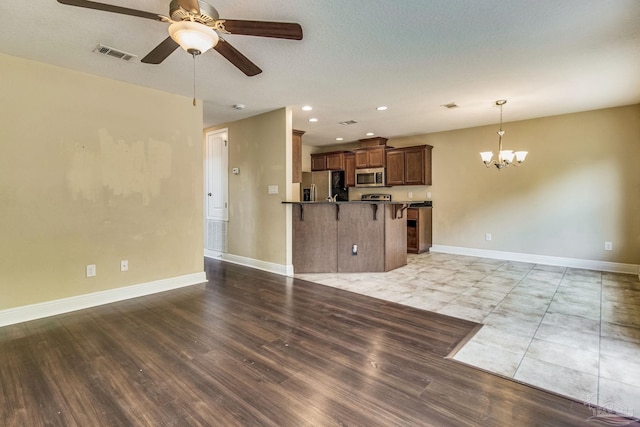 unfurnished living room featuring ceiling fan with notable chandelier and light wood-type flooring