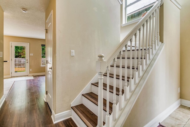 stairs featuring wood-type flooring, plenty of natural light, and a textured ceiling