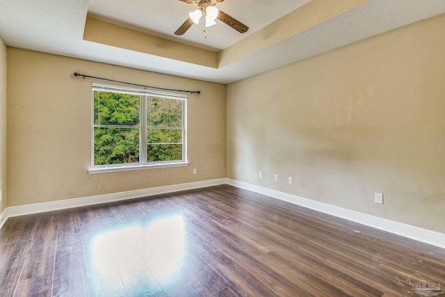 empty room with a tray ceiling, dark hardwood / wood-style floors, and ceiling fan