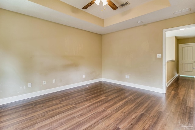 unfurnished room featuring dark wood-type flooring, ceiling fan, and a tray ceiling