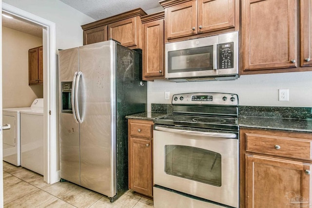 kitchen with light tile patterned flooring, appliances with stainless steel finishes, washer and dryer, and dark stone countertops