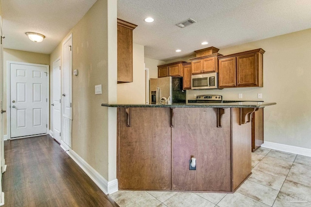 kitchen with appliances with stainless steel finishes, a breakfast bar, kitchen peninsula, and a textured ceiling