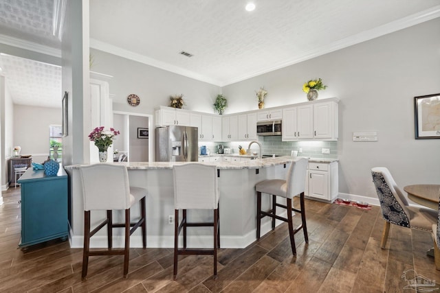1328 Tour Dr, Gulf Breeze, FL 32563 - kitchen featuring stainless steel appliances, a kitchen bar, white cabinetry, dark wood finished floors, and tasteful backsplash