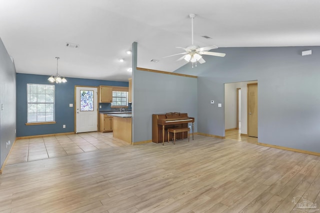 unfurnished living room featuring ceiling fan with notable chandelier, a wealth of natural light, light hardwood / wood-style floors, and vaulted ceiling