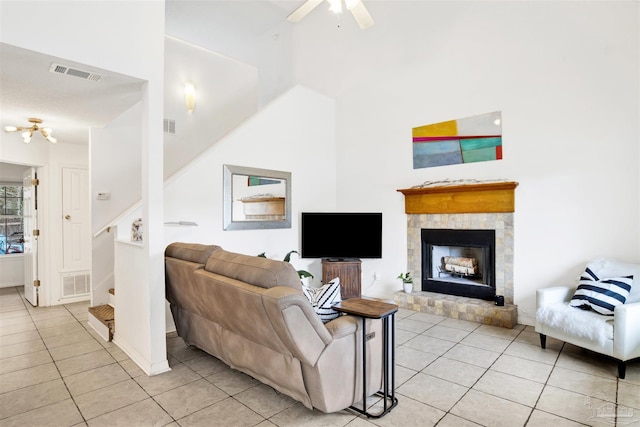 tiled living room with ceiling fan, a fireplace, and a high ceiling