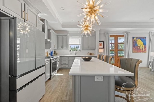 kitchen featuring gray cabinetry, wall chimney range hood, light hardwood / wood-style flooring, appliances with stainless steel finishes, and a kitchen island